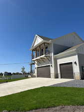 View of front of property with board and batten siding, driveway, a balcony, a front lawn, and a shingled roof