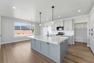 Kitchen with a barn door, stainless steel range with gas cooktop, light wood finished floors, a center island with sink, and tasteful backsplash