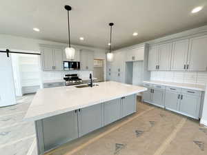 Kitchen featuring gray cabinets, a barn door, backsplash, light stone counters, and decorative light fixtures