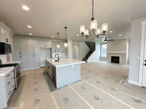 Kitchen with a chandelier, appliances with stainless steel finishes, a fireplace, pendant lighting, and a kitchen island with sink