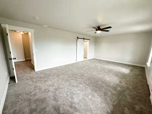 Unfurnished bedroom with a barn door, carpet flooring, and a ceiling fan