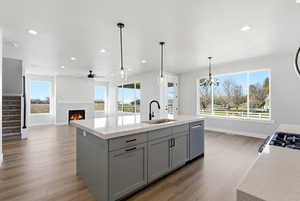 Kitchen featuring a lit fireplace, gray cabinetry, a kitchen island with sink, light wood-style flooring, and hanging lights