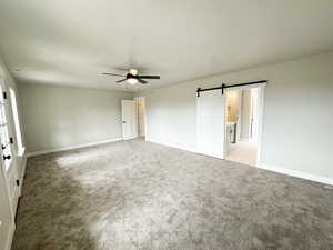 Unfurnished bedroom featuring a barn door, light carpet, and a ceiling fan