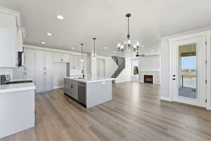 Kitchen featuring hanging lights, a center island with sink, open floor plan, a warm lit fireplace, and gray cabinets