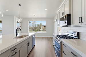 Kitchen featuring stainless steel appliances, light stone countertops, light wood-type flooring, tasteful backsplash, and suspended lighting