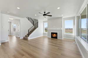 Unfurnished living room featuring a ceiling fan, a warm lit fireplace, recessed lighting, and light wood-type flooring