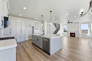 Kitchen with a lit fireplace, a center island with sink, open floor plan, stainless steel appliances, and light wood finished floors