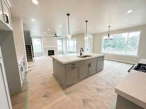 Kitchen with a glass covered fireplace, light stone counters, pendant lighting, an island with sink, and ceiling fan