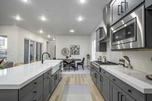 Kitchen featuring light hardwood / wood-style flooring, plenty of natural light, sink, appliances with stainless steel finishes, and a center island with sink