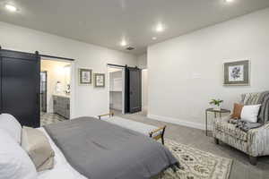 Bedroom featuring a barn door, connected bathroom, and light carpet