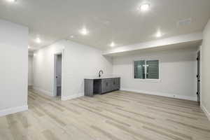 Basement featuring a textured ceiling, sink, and light hardwood / wood-style floors