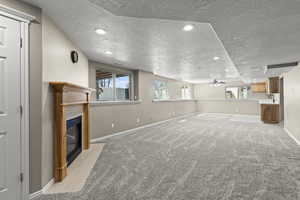 Unfurnished living room featuring baseboards, a textured ceiling, a fireplace with flush hearth, and ceiling fan