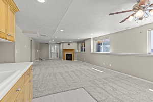Unfurnished living room with ceiling fan, a textured ceiling, a fireplace, light carpet, and recessed lighting