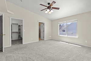 Unfurnished bedroom with carpet floors, baseboards, a walk in closet, a ceiling fan, and vaulted ceiling