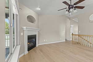 Unfurnished living room featuring a glass covered fireplace, wood finished floors, lofted ceiling, baseboards, and a ceiling fan