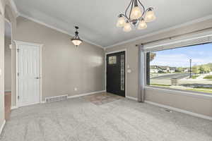 Foyer featuring an inviting chandelier, ornamental molding, carpet, and visible vents