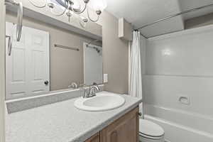 Full bathroom with shower / bath combo with shower curtain, toilet, a textured ceiling, and vanity