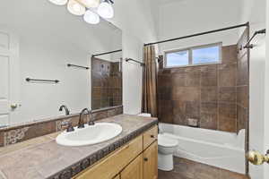 Bathroom featuring shower / bath combo with shower curtain, stone finish flooring, toilet, and vanity