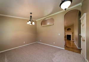 Carpeted spare room featuring crown molding and a chandelier