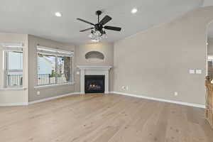 Unfurnished living room featuring a glass covered fireplace, baseboards, ceiling fan, a textured ceiling, and light wood-style flooring