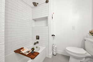 Bathroom featuring tile patterned flooring, tiled shower / bath combo, and toilet