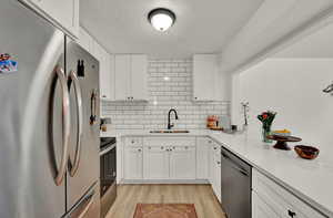 Kitchen with stainless steel appliances, light hardwood / wood-style floors, tasteful backsplash, sink, and white cabinets