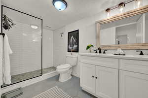 Ensuite bathroom with tile patterned floors, a tile shower, double vanity, and toilet