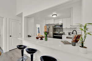 Kitchen with kitchen peninsula, light hardwood / wood-style flooring, appliances with stainless steel finishes, and backsplash