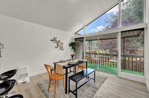 Dining area featuring vaulted ceiling, light wood-style flooring, and large mid-century windows