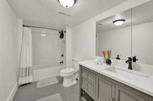 Full bathroom with toilet, vanity, shower / bath combo, tile patterned floors, and a textured ceiling