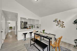 Dining area featuring sink, high vaulted ceiling, a textured ceiling, and light hardwood / wood-style floors