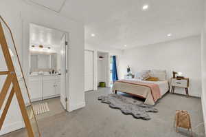 Bedroom with  ensuite bathroom, light colored carpet, and canned lights