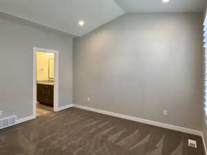 Unfurnished bedroom featuring lofted ceiling, light colored carpet, and ensuite bath