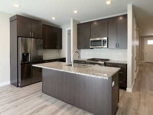 Kitchen with sink, appliances with stainless steel finishes, light hardwood / wood-style flooring, dark brown cabinets, and decorative backsplash