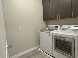 Clothes washing area with washing machine and dryer, cabinets, and light wood-type flooring