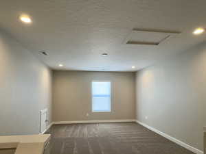 Unfurnished room with a textured ceiling and dark colored carpet