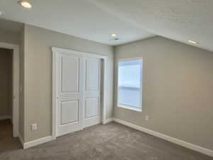 Unfurnished bedroom featuring a textured ceiling, carpet floors, lofted ceiling, and a closet