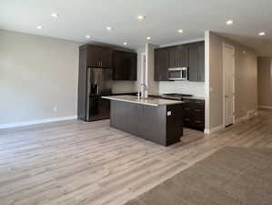 Kitchen featuring light hardwood / wood-style flooring, dark brown cabinets, tasteful backsplash, stainless steel appliances, and a center island with sink