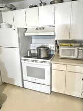 Kitchen featuring white appliances, premium range hood, and white cabinets