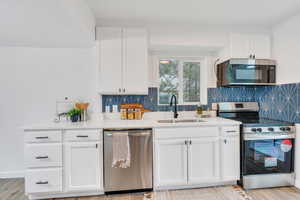 Kitchen featuring light wood-type flooring, tasteful backsplash, white cabinetry, appliances with stainless steel finishes, and sink