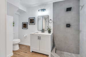 Downstairs 3/4 Bathroom featuring wood-type flooring, a tile shower, vanity, and toilet