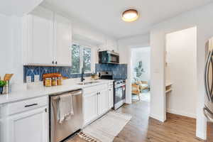 Kitchen with appliances with stainless steel finishes, light hardwood / wood-style flooring, tasteful backsplash, sink, and white cabinets