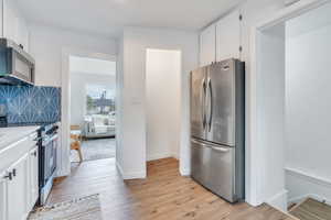 Kitchen with white cabinetry, backsplash, light hardwood / wood-style flooring, and appliances with stainless steel finishes and a large pantry