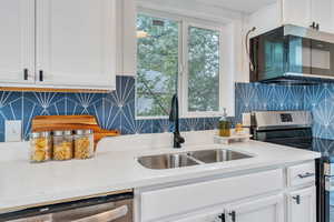 Kitchen with white cabinets, sink, backsplash, and stainless steel appliances