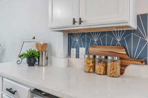 Details featuring white cabinetry, decorative backsplash, and light stone counters