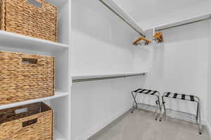 Primary Bedroom walk-in closet with self basket organizers and luggage racks