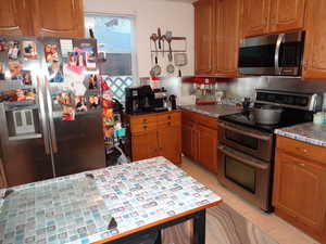 Kitchen with decorative backsplash, appliances with stainless steel finishes, and light tile patterned flooring