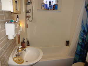 Full bathroom with sink, tile walls, shower / tub combo with curtain, and toilet