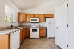 Kitchen with light tile patterned flooring, sink, white appliances, and lofted ceiling