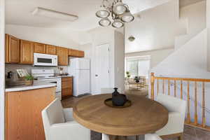 Kitchen featuring lofted ceiling, dark tile patterned floors, a chandelier, and white appliances. Virtually staged